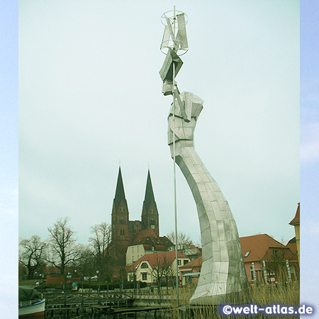 Die Großplastik Parzival am See in Neuruppin am Ruppiner See, dahinter die Türme der Klosterkirche St. Trinitatis 