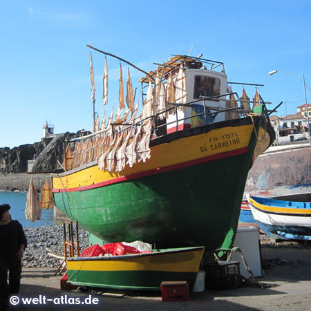 Fischerboote am Hafen von Câmara de Lobos, Stockfisch trocknet an Holzgestellen in der Sonne