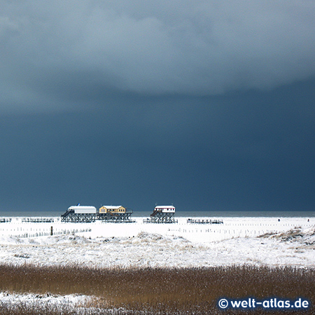 Dramatischer Himmel und Wolkenbildung im Winter in St. Peter-Ording, Bilck über das Vorland und den Strand auf die Pfahlbauten am Meer