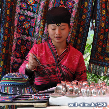Yao Frau in der traditionellen roten Tracht, im Hintergrund sieht man die schönen Textilien und typischen Muster