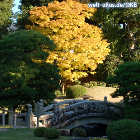 Japanischer Garten im Herbstlaub mit alter Steinbrücke 