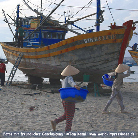 Frauen am Ufer und Fischerboot in Mui Ne