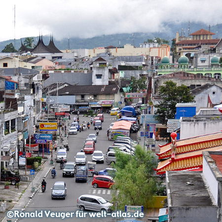 Blick von der Brücke auf das lebendige Leben in der Straße Jalan Ahmad Yani der Stadt Bukittinggi – im Hintergrund ist der Mount Merapi hinter Wolken verschwunden